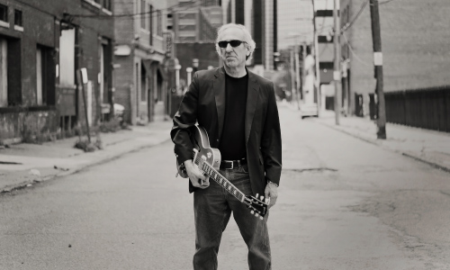 John Hern standing in middle of street holding guitar